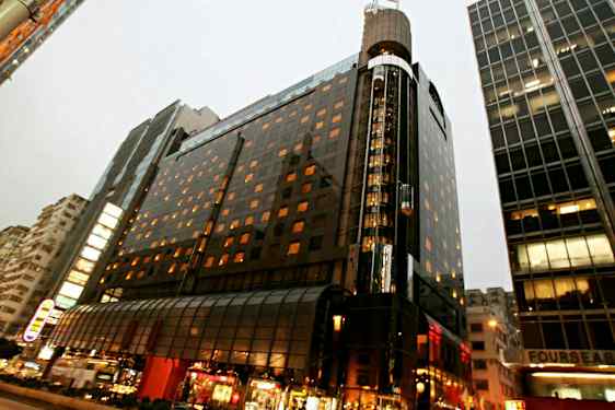 En oplyst fleretagers bygning i et bymiljø med glasfacade og gadeliv i forgrunden. (AI-genereret tekst)