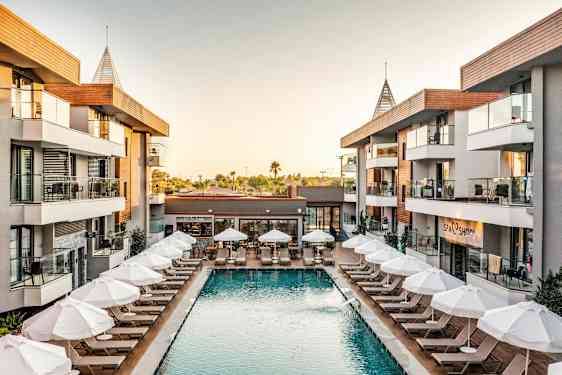 Hotelområde med pool og liggestole omgivet af bygninger. (AI-genereret tekst)