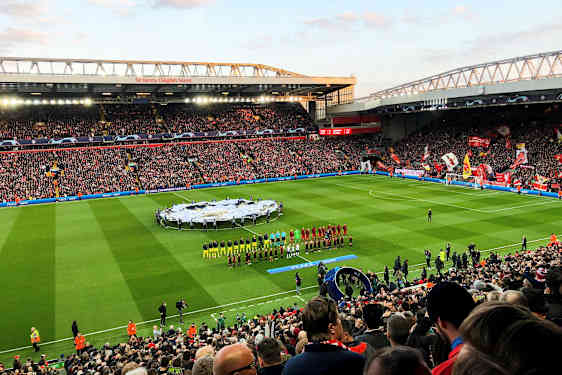 Fodboldstadion fyldt med tilskuere, spillere og personale på banen før en kamp. (AI-genereret tekst)