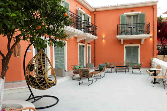 En gårdhave med stole og borde foran en bygning med orange facade og grønne skodder. (AI-genereret tekst)