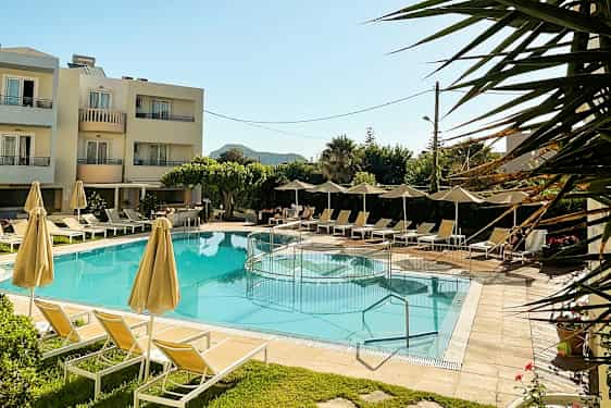 Udendørs pool med liggestole og parasoller, omgivet af grønne områder og et hotel i baggrunden. (AI-genereret tekst)