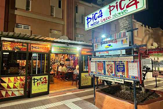 En restaurant ved navn Pica Pica ses om natten. Skilte og menuer pryder eksteriøret. (AI-genereret tekst)