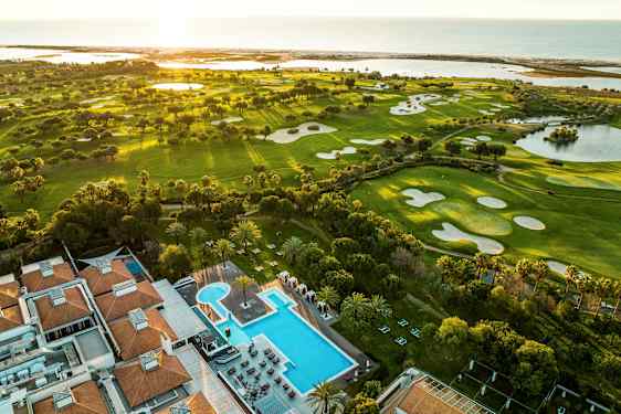 Luftfoto af golfbaner og et hotel med poolområde. (AI-genereret tekst)