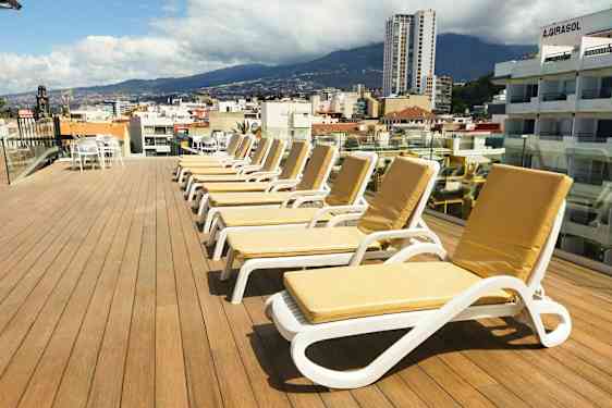 En tagterrasse med liggestole og udsigt over en by og omkringliggende bjerge. (AI-genereret tekst)