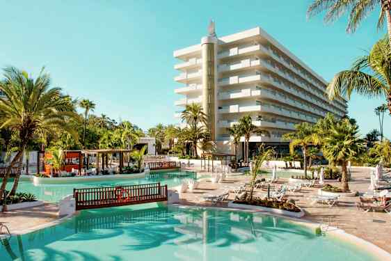 Hotel med poolområde, liggestole og palmer. (AI-genereret tekst)