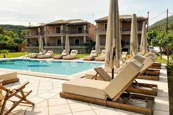 Udendørs pool med liggestole og parasoller, omgivet af bygninger og grønne områder. (AI-genereret tekst)