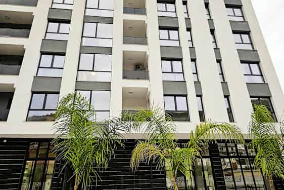 Boligbygning med glasfacade og altaner, omgivet af palmer. (AI-genereret tekst)