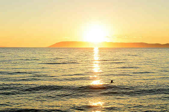 Solnedgang over havet med en silhuet af en svømmende person. (AI-genereret tekst)