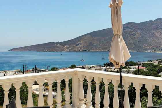 En udsigt fra en terrasse med rækværk, en parasol og havet og bjerge i baggrunden. (AI-genereret tekst)