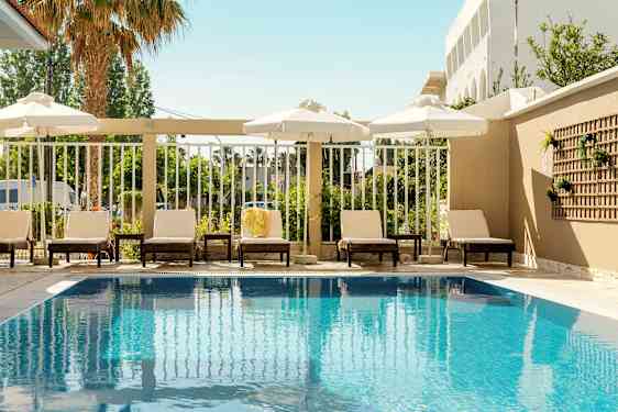 Udendørspool med liggestole og parasoller langs kanten. (AI-genereret tekst)