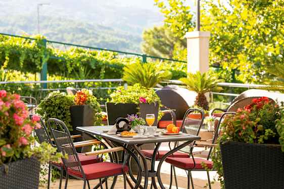 Bord med røde stole omgivet af grønne planter og farverige blomster. (AI-genereret tekst)