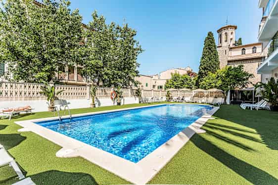 Udendørs pool med liggestole omkring, omgivet af landsbyarkitektur og grønne områder. (AI-genereret tekst)