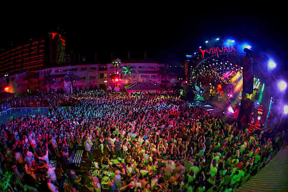 En natklub med et publikum foran en farverigt oplyst scene. (AI-genereret tekst)