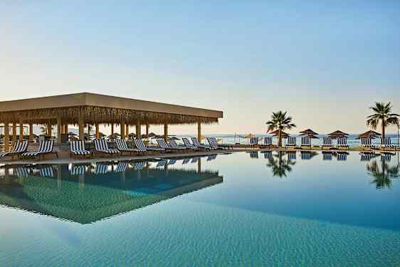 En udendørs swimmingpool med liggestole og parasoller ved havet. (AI-genereret tekst)