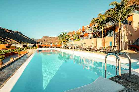 Udendørs pool ved et hotel med liggestole og bjerge i baggrunden. (AI-genereret tekst)