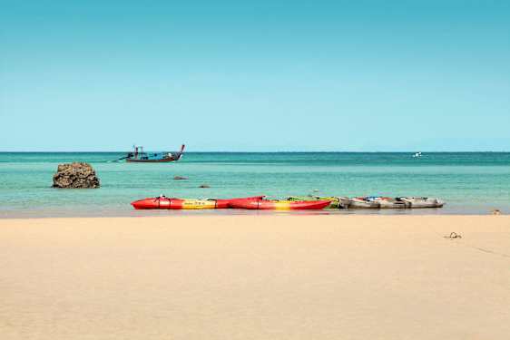 Flere kajakker på en sandstrand, med havet og en båd i baggrunden. (AI-genereret tekst)