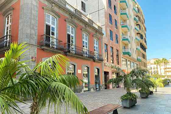 Udvendig kig på et hotel med altaner og vinduer, omgivet af palmer og en stenbelagt gangsti. (AI-genereret tekst)