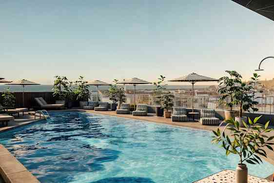 Udendørs swimmingpool med parasoller, liggestole og planter omkring. (AI-genereret tekst)