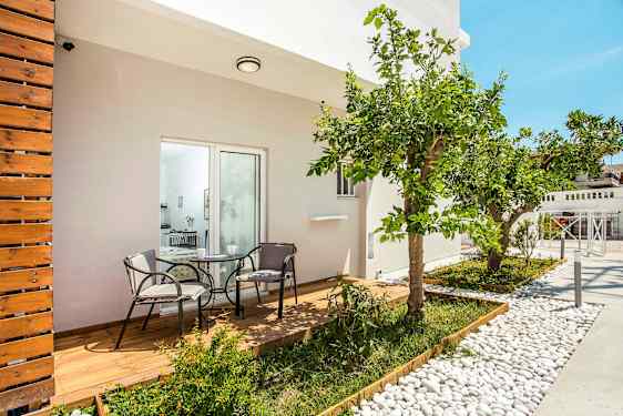 En terrasse med træterrasse og to stole omkring et bord, omgivet af planter og et citrus træ. (AI-genereret tekst)