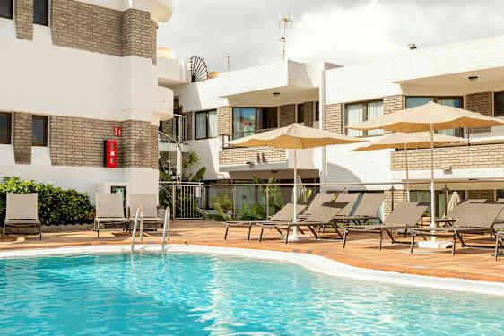 Udendørs poolområde med liggestole og parasoller ved en bygning. (AI-genereret tekst)