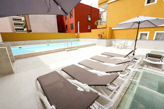 Udendørs pool med liggestole og parasoller på et stenbelagt område. (AI-genereret tekst)