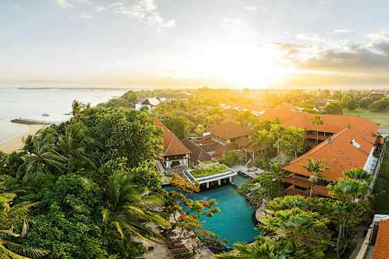 Et udendørs billede af et tropisk hotelområde med pool og havet i baggrunden ved solopgang. (AI-genereret tekst)