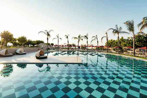 En udendørs pool med ternet mønster, omgivet af palmer og liggestole. (AI-genereret tekst)