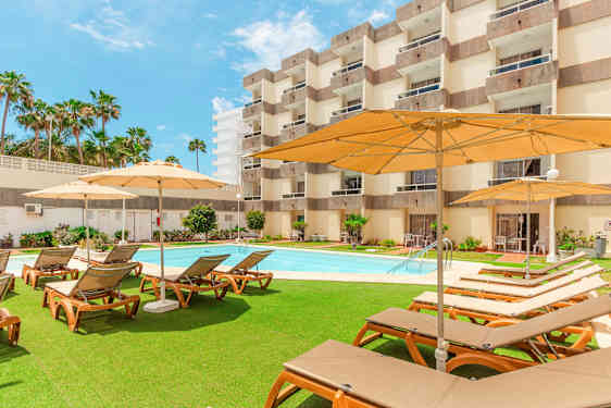 Udendørsområde med liggestole, parasoller og pool foran et hotel. (AI-genereret tekst)