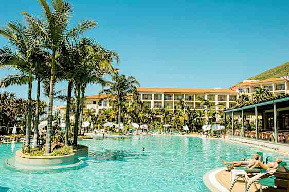 Opvarmet udendørs pool omgivet af palmetræer ved hotel med flere etager. (AI-genereret tekst)