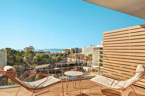 Udsigt over et bymiljø med hoteller og grønne områder fra en altan med siddepladser. (AI-genereret tekst)