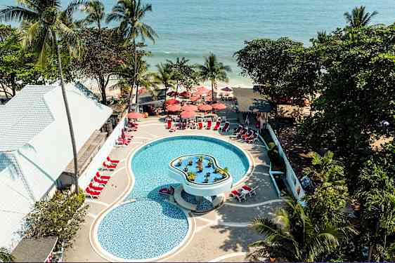 Luftfoto af en pool på et feriested med liggestole og parasoller, omgivet af tropiske træer og tæt på havet. (AI-genereret tekst)