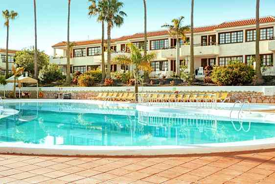 En swimmingpool omgivet af liggestole med en hvid bygning i baggrunden. (AI-genereret tekst)