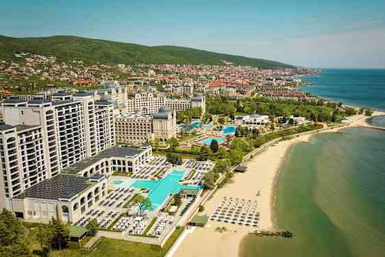 Hoteller og pools ved stranden med havet og byen i baggrunden. (AI-genereret tekst)