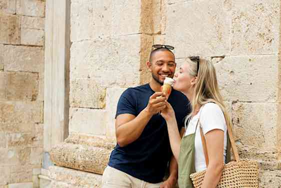 To personer står ved en stenbygning, hvor den ene har en stråtaske. (AI-genereret tekst)