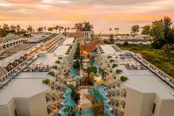 Luftfoto af hotelkompleks med poolområde og solnedgang i baggrunden. (AI-genereret tekst)