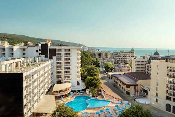 Hotelbygninger med en udendørs pool og solsenge, omgivet af andre bygninger tæt på havet. (AI-genereret tekst)