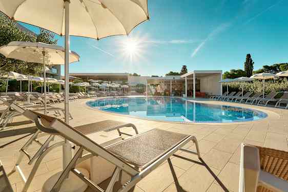 En udendørs swimmingpool omgivet af liggestole og parasoller under en klar blå himmel. (AI-genereret tekst)