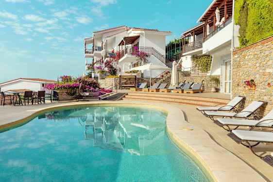 Udendørs pool ved hotel bygget i middelhavsstil med liggestole og blomster. (AI-genereret tekst)