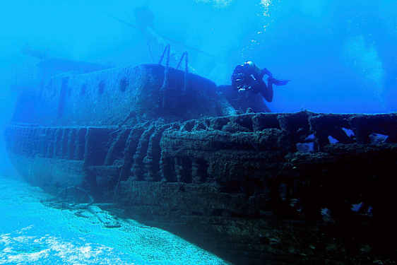 Et undervandsfotografi af et sunket skib med en dykker, der svømmer ved siden af. (AI-genereret tekst)