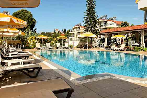 En udendørs pool med liggestole og parasoller, omgivet af grønne områder og bygninger. (AI-genereret tekst)