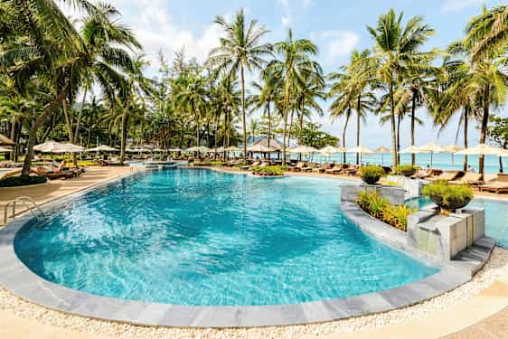 En udendørs pool omgivet af liggestole og parasoller ved en tropisk resort. (AI-genereret tekst)