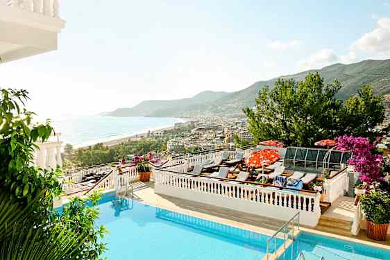 Udsigt over en pool med liggestole, havet og en kystby i baggrunden. (AI-genereret tekst)