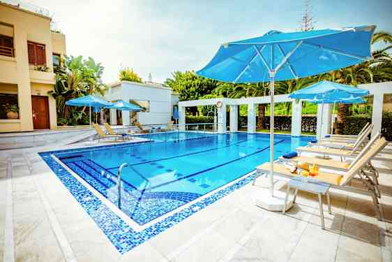 En udendørs pool med blå parasoller og liggestole omkring. (AI-genereret tekst)