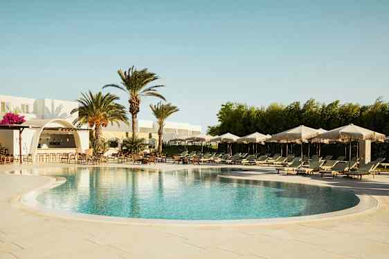 En udendørs pool med liggestole og parasoller, omgivet af palmer og en bygning med en bar. (AI-genereret tekst)