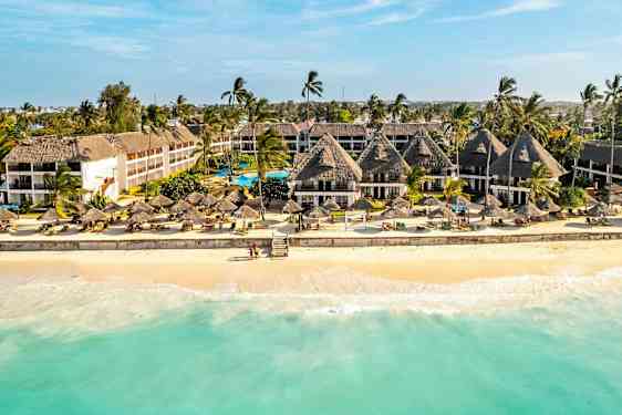 Hotel ved en sandstrand med palmer og parasoller. (AI-genereret tekst)