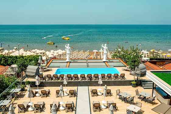 Udsigt over en pool med liggestole, statuer og en sandstrand ved havet. (AI-genereret tekst)