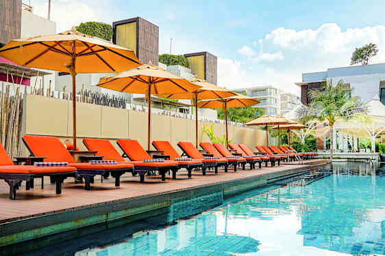 En udendørs pool med orange solsenge og parasoller ved kanten, omgivet af moderne arkitektur. (AI-genereret tekst)