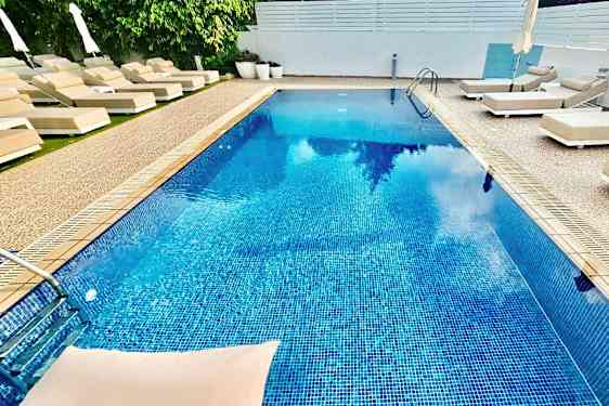 Udendørs pool omgivet af liggestole og parasoller. (AI-genereret tekst)