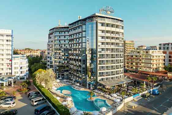 Et fler-etagers hotel med pool og liggestole foran, beliggende i et tætbebygget område. (AI-genereret tekst)