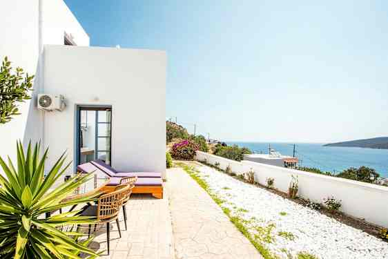 Hvid bygning med liggestole og bord på en terrasse med udsigt over havet. (AI-genereret tekst)